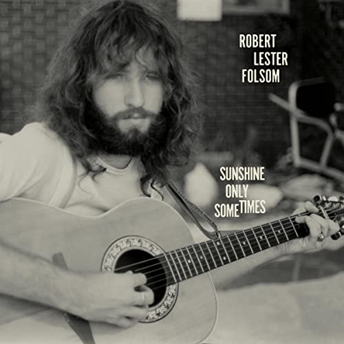 Black and white portrait of a long-haired man playing an acoustic guitar.