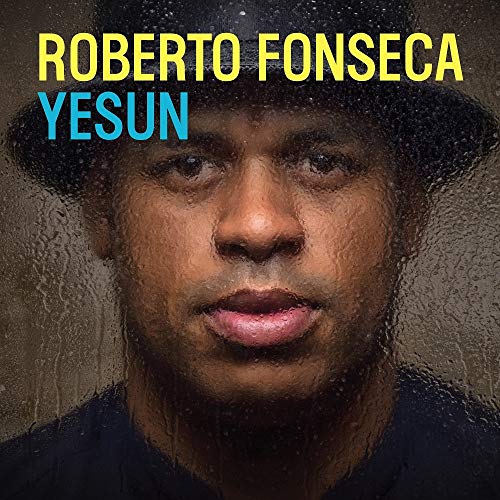 Portrait of Roberto Fonseca wearing a hat, seen through a rain-streaked glass surface.