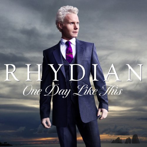Man in blue suit and purple tie stands against cloudy sky, "RHYDIAN One Day Like This" text overlay.