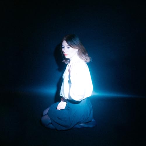 Woman kneeling in darkness, illuminated by a blue light source.