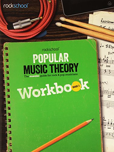 Green spiral-bound Rockschool Grade 3 music theory workbook with a pencil and musical accessories.