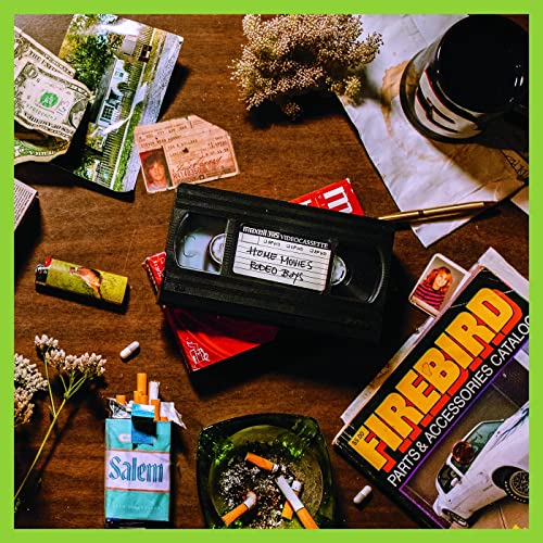 Vinyl record cover with a VHS tape, cigarettes, and scattered ephemera.