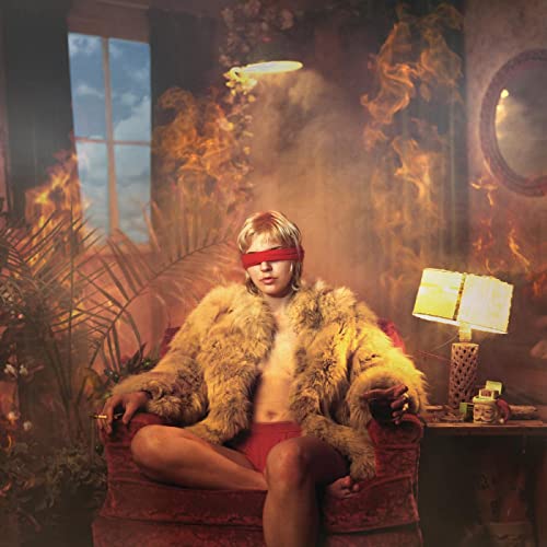 Person in faux fur, blindfolded, sitting in a room with smoke.
