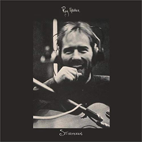 Black and white portrait of Roy Harper wearing headphones and playing an acoustic guitar.