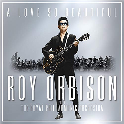 Roy Orbison wearing sunglasses and holding a guitar in front of an orchestra.