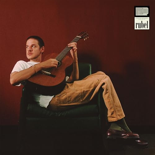 Man with guitar sitting in chair against a red background.