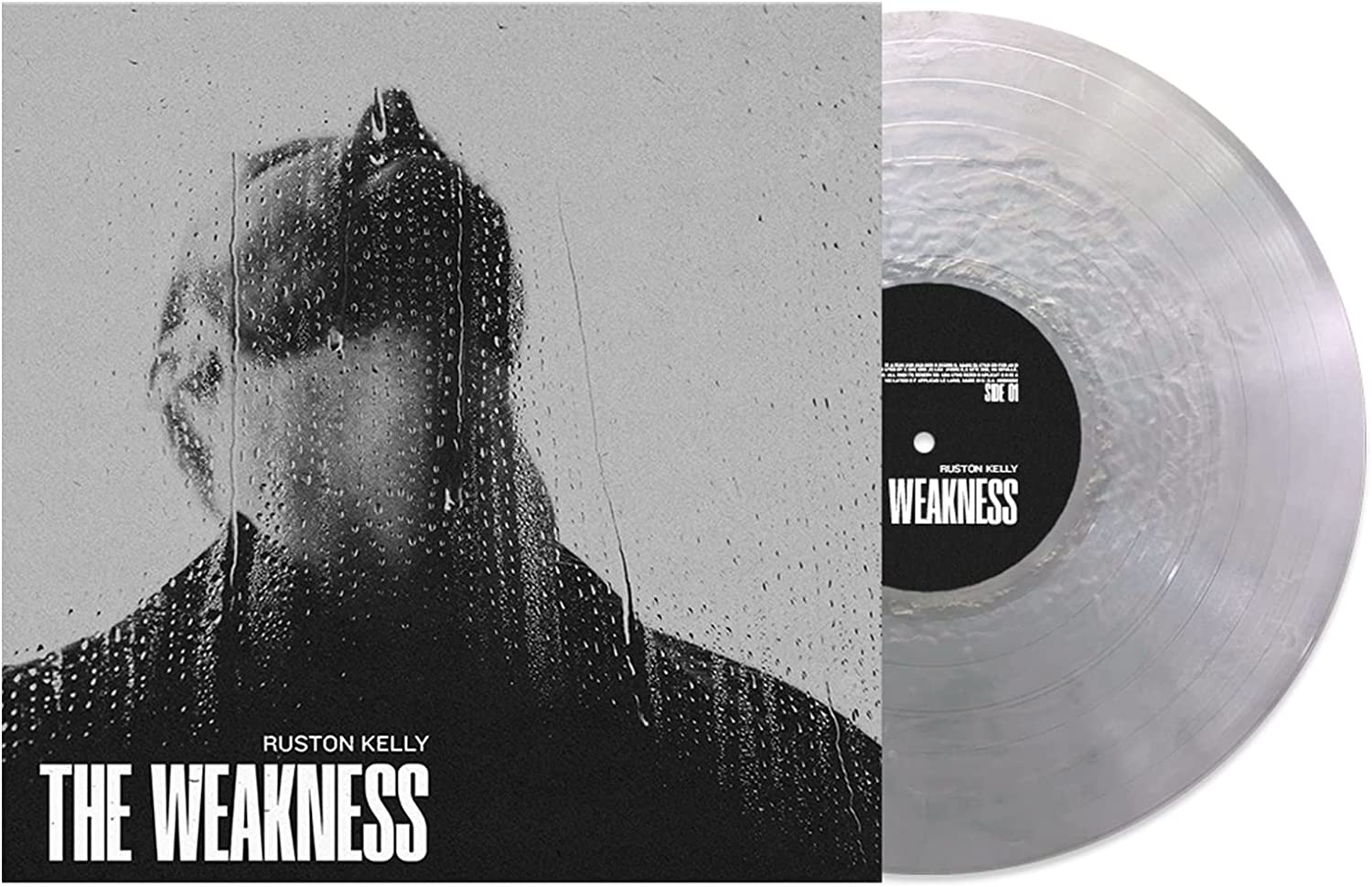 A vinyl record with a clear disc and a black label, alongside its album cover.