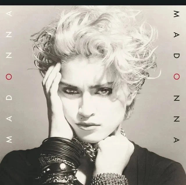 Black and white portrait of Madonna with curly hair wearing stacked bracelets and necklaces.