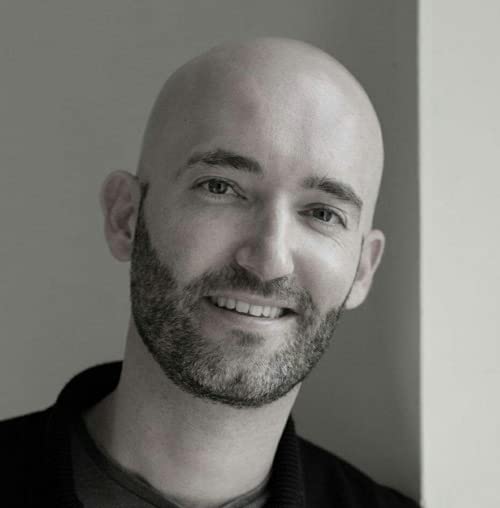 Black and white portrait of a smiling bald man with a short beard.