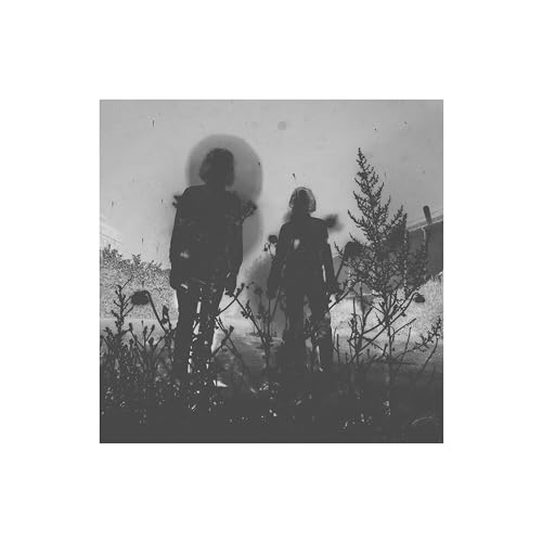 Black and white photo of two figures standing in overgrown foliage.
