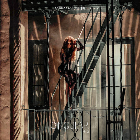 Sabrina Carpenter standing on a fire escape in a black lace dress at night.