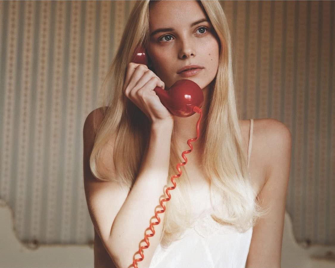 Woman with long blonde hair holding a red rotary phone.