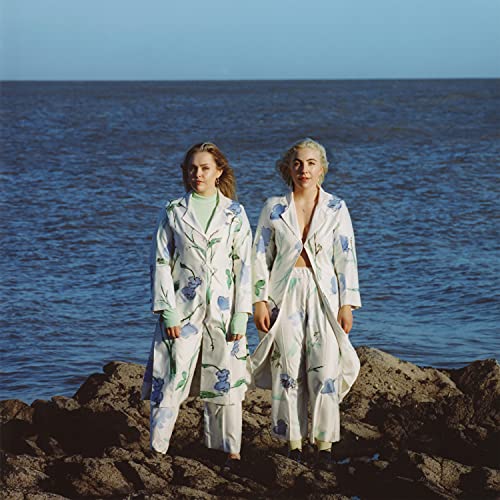 Two women in floral patterned clothing stand by a rocky shore.