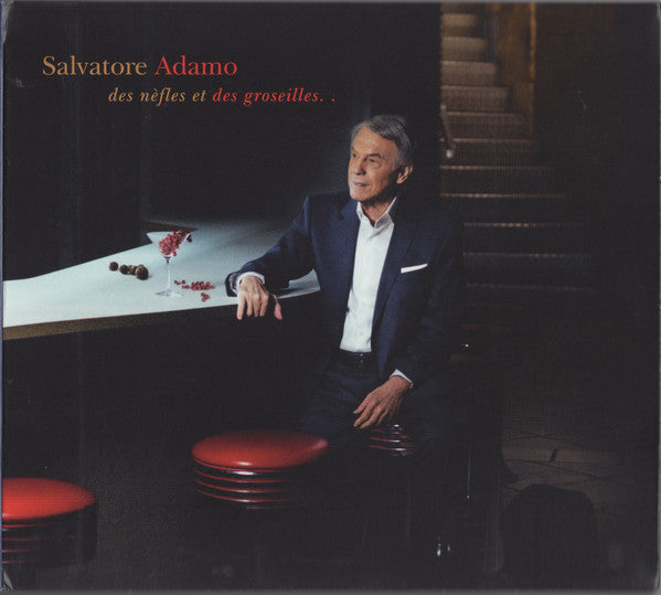 Salvatore Adamo sits in a dark room with red stools and a table.