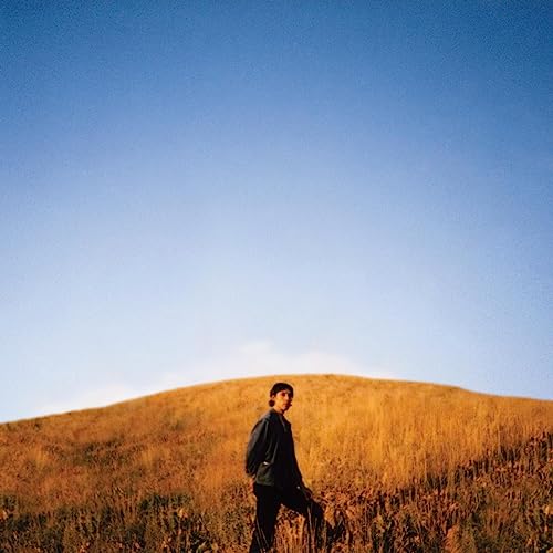 CD cover: Man walking on a grassy hill under a blue sky.