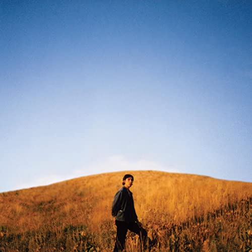 Man walking on a grassy hill under a clear blue sky.