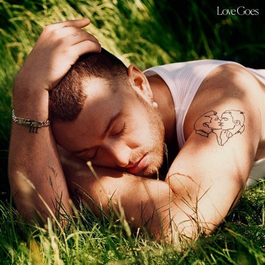 Man lying in grass with eyes closed, wearing white tank top, with arm tattoo visible.