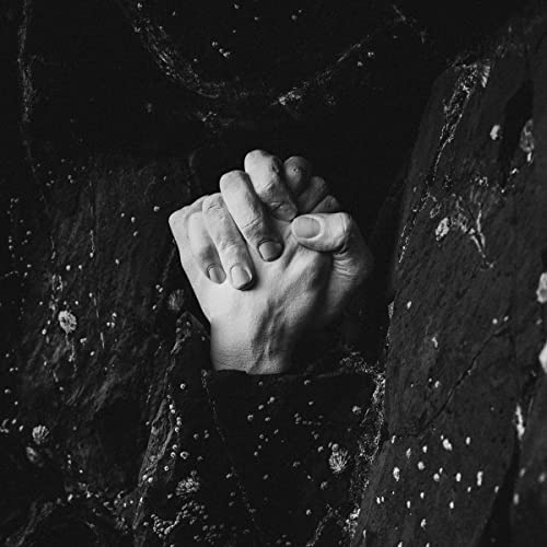 A black-and-white image of clasped hands against a dark, rocky background.