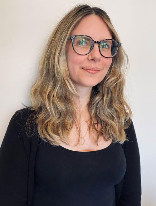 Woman with wavy blonde hair and glasses, looking at the camera.