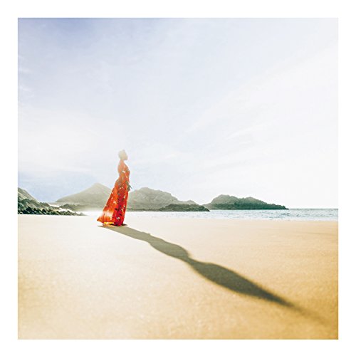 Woman in red dress standing on beach, mountains in background.