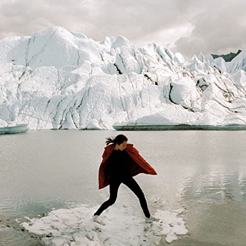 Woman in red jacket poses before a snowy mountain landscape.