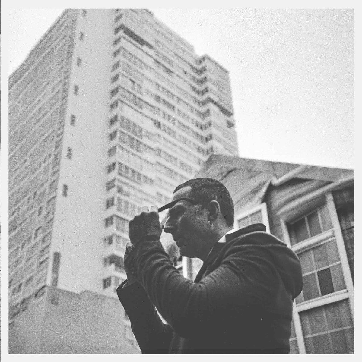 Black and white photo of a man in glasses looking up at a tall building.