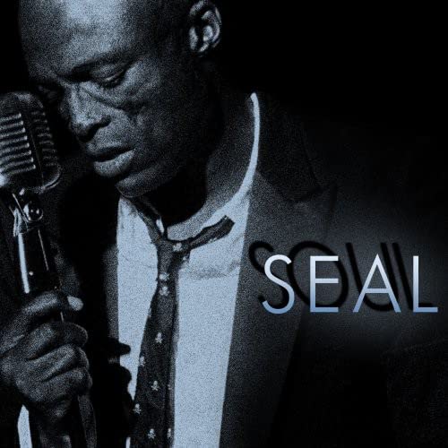 Close-up of Seal singing into a vintage microphone, dark blue background.