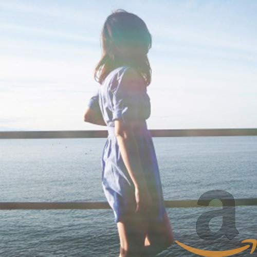 Woman with long hair standing by the ocean, back to viewer.