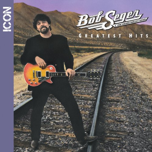 Bob Seger standing on train tracks holding a guitar, mountains in the background.