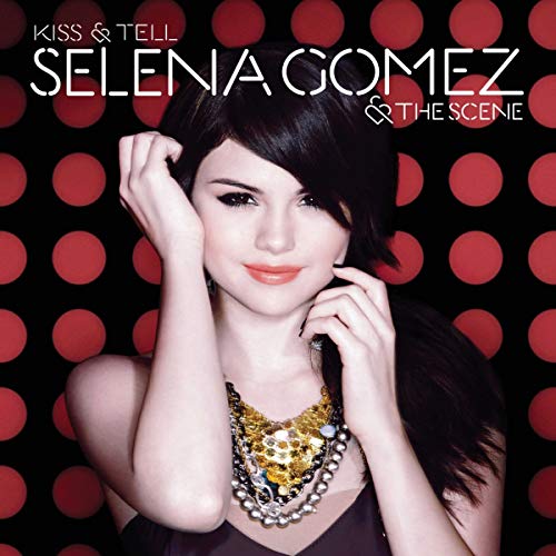 Selena Gomez with dark hair wearing a gold necklace against a red polka-dot background.