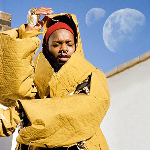 Serpentwithfeet in yellow hooded garment, moons and blue sky backdrop.