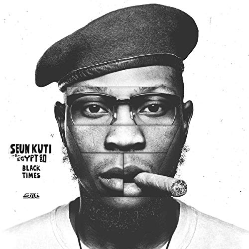 Black and white portrait of Seun Kuti wearing a beret and smoking a cigar.