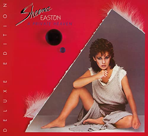 Sheena Easton sits on a grey surface against a red background with white feathers.