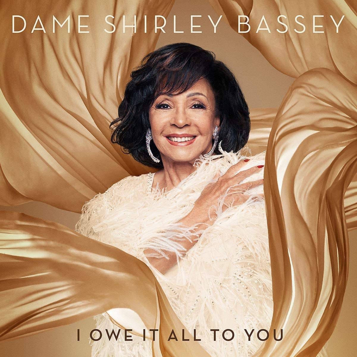 "CD cover featuring Dame Shirley Bassey in a white dress surrounded by gold fabric."