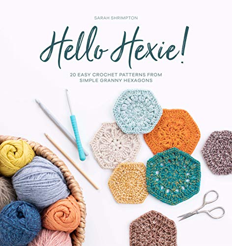 Crochet book cover with yarn, hexagons, and tools on a white surface.