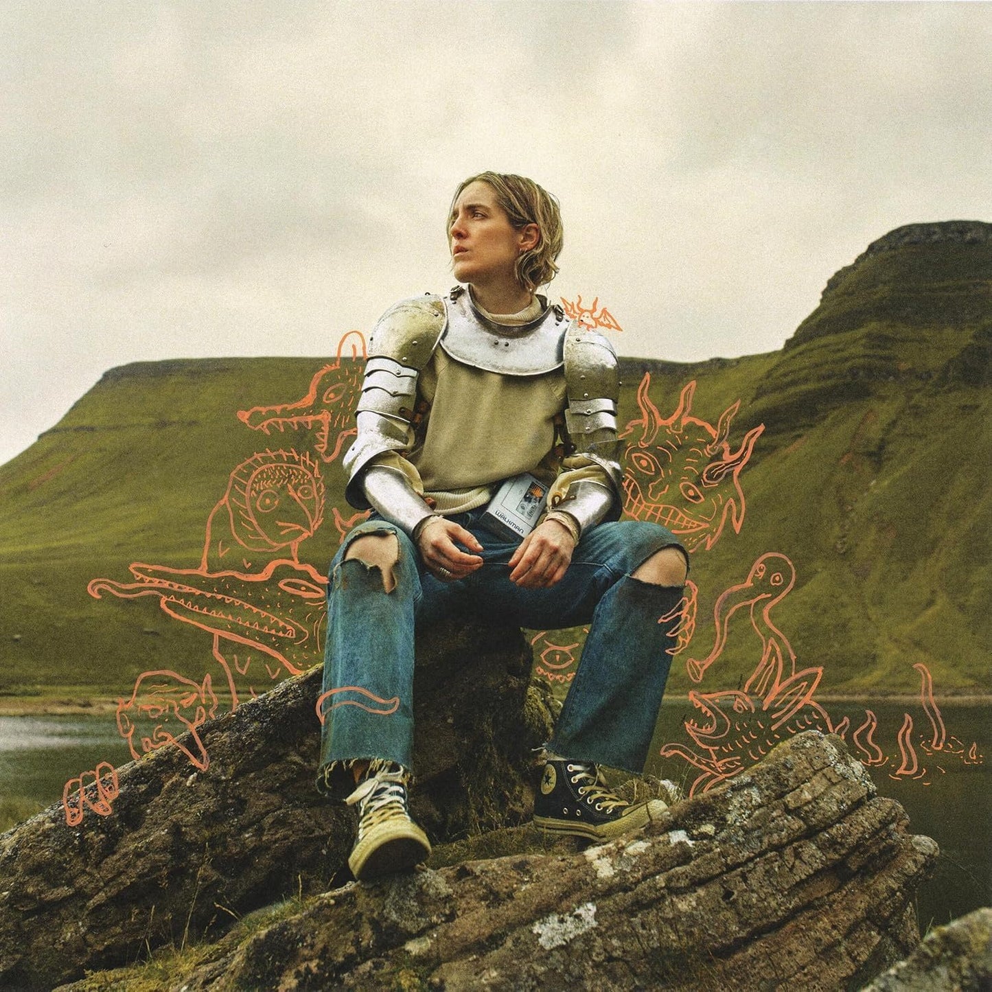 Person in jeans and armor sits on rocks with sketched dragons.