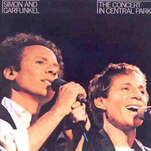 The image shows Simon and Garfunkel singing into microphones on a dark background.