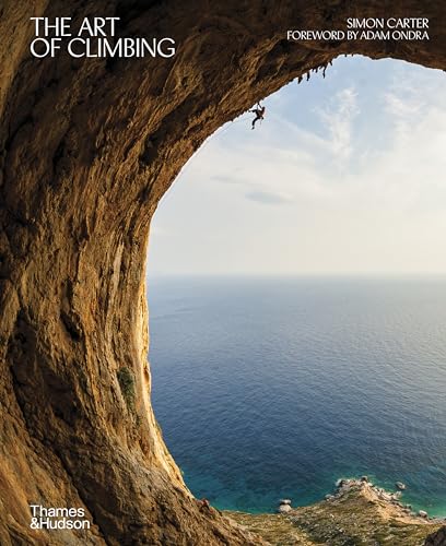 A rock climber hangs from a cave ceiling overlooking the ocean.
