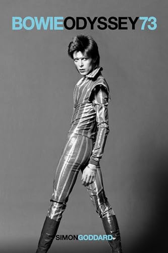 Black and white portrait of David Bowie wearing a striped jumpsuit and tall boots.