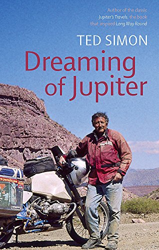 A man in a red jacket stands next to his motorcycle in a desert landscape.
