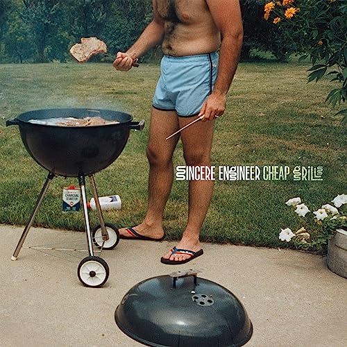 Man grilling meat over a charcoal grill on a lawn.