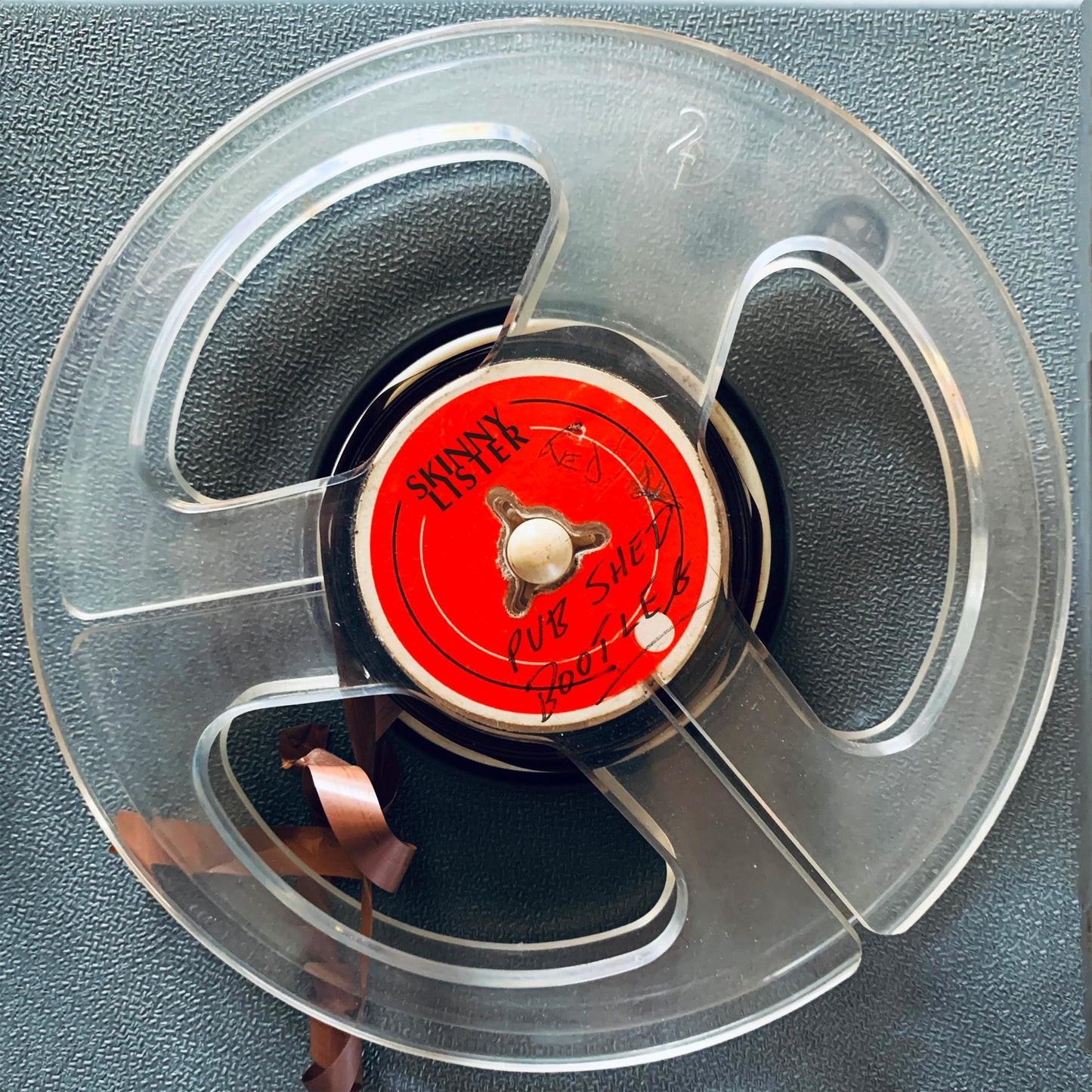 Clear plastic reel-to-reel tape with a red center label reading Skinny Lister Pub Shed.