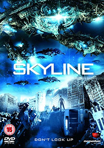 Alien spaceships hover over a ruined city with a lone figure standing in rubble.