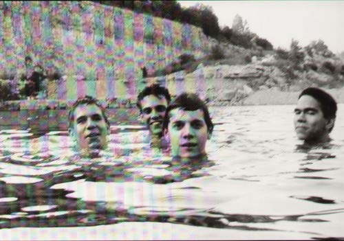 Four men swimming in a quarry with a digital color-shifting glitch effect overlay.