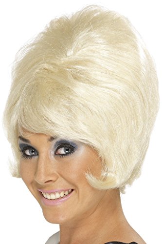 A woman wearing a blonde beehive wig, smiling, with heavy eye makeup.