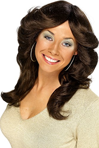 A woman wearing a brown, curly wig and beige top, smiling at the camera.
