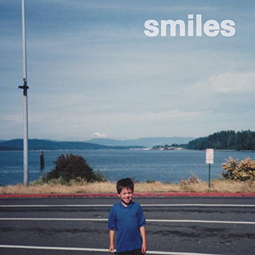 "Album cover with a young boy standing on a road near a body of water."