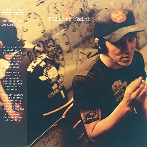 Elliott Smith wearing a baseball cap in front of a graffiti-covered wall.