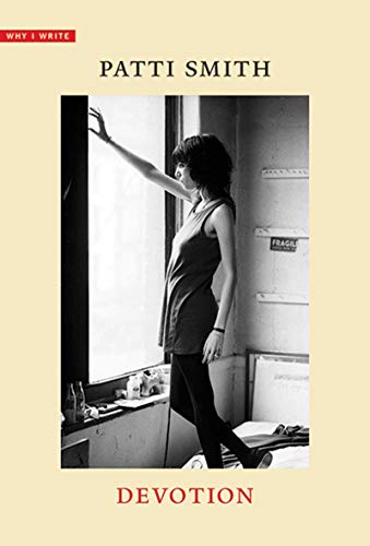Black and white photo of woman in dark clothing standing by a window.