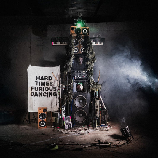 Dark room with tangled electronics and fog, sign reading Hard Times Furious Dancing.